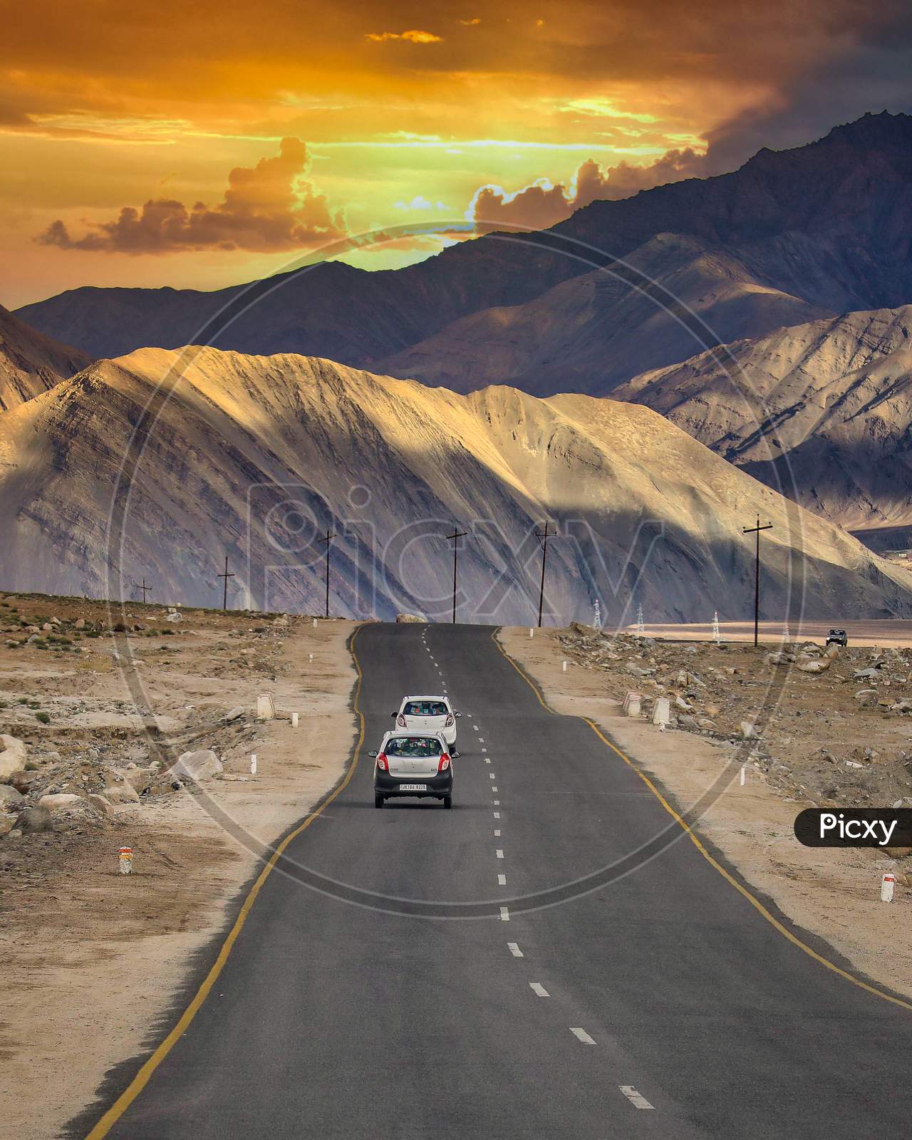 Vehicles on NH1 Road In Leh With Snow Filed Mountains in Background And Sunset Sky