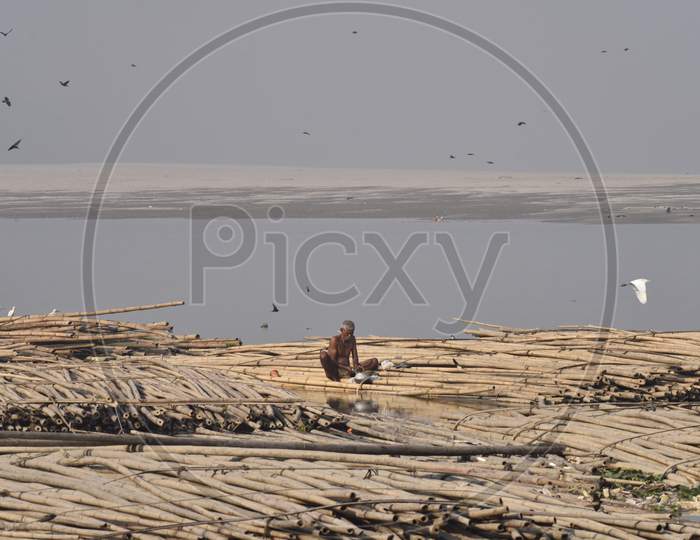 A Man  Washing Clothes By Sitting on Floating Bamboo Boards or Boats Over Bramhaputra River In Assam