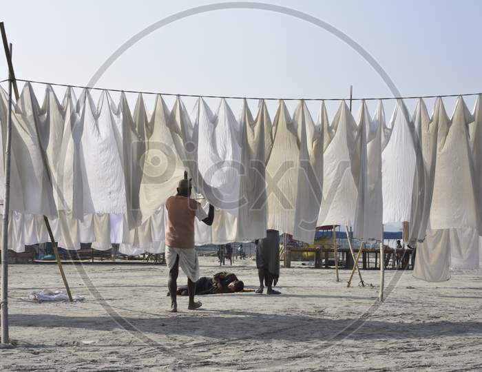 Indian Washer Man or Dhobi Drying Washed Clothes on The Bank Of Bramhaputra River In Assam