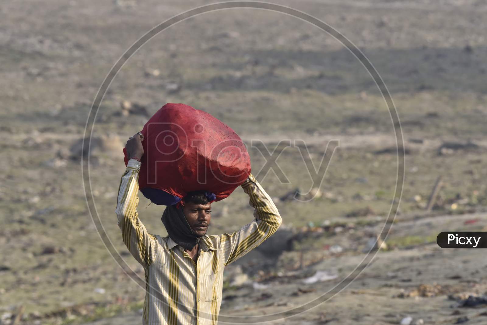 Indian Washer Man Carrying Clothes Bundles over His head on Bramhaputra River Bank In Assam