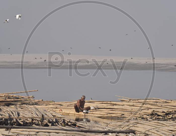 A Man  Washing Clothes By Sitting on Floating Bamboo Boards or Boats Over Bramhaputra River In Assam