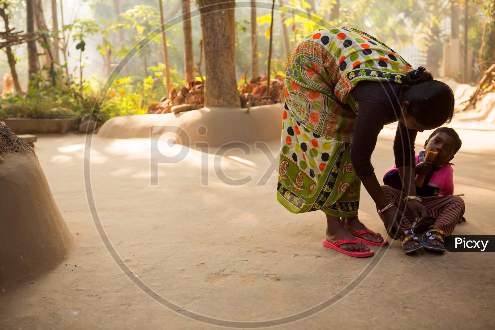 Birbhum, West Bengal, India February 7th 2015 : In a village of West Bengal a Santhal tribe woman helping her kid to tie the shoe at her neat and clean courtyard