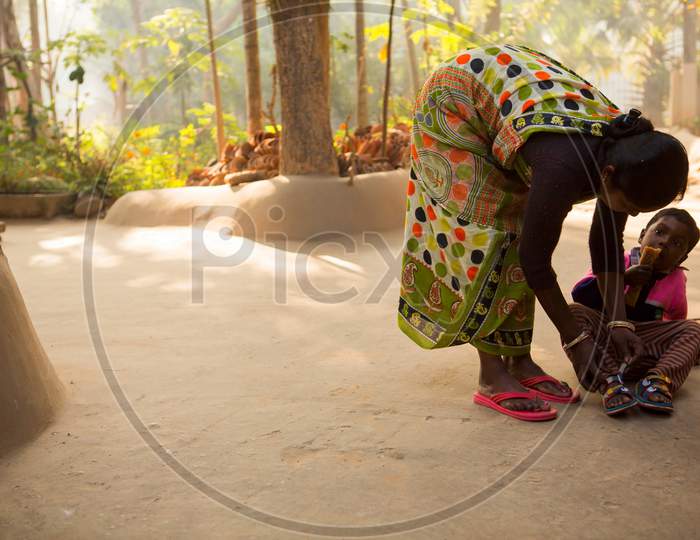 Birbhum, West Bengal, India February 7th 2015 : In a village of West Bengal a Santhal tribe woman helping her kid to tie the shoe at her neat and clean courtyard