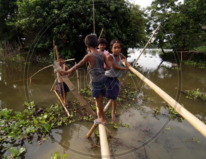 Children Cross Flood Waters Through A Bamboo Bridge In The Flood Affected Morigaon District Of Assam State, India, On July 22,2016