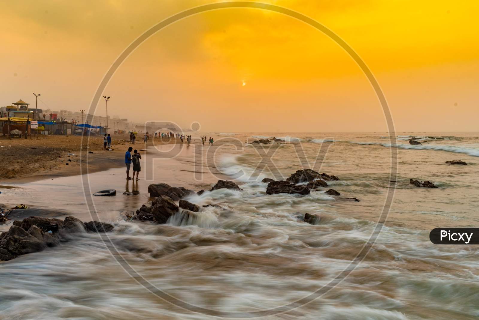 Long Exposure Of People In an Beach With Smooth Waves Transition  And Golden Sunset Sky in Background