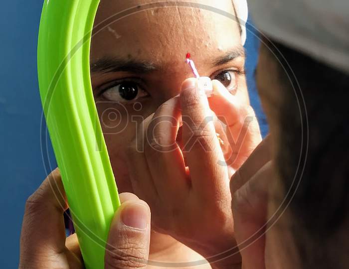 An Indian Woman Putting On Vermilion on Forehead by Looking Into an Hand Mirror