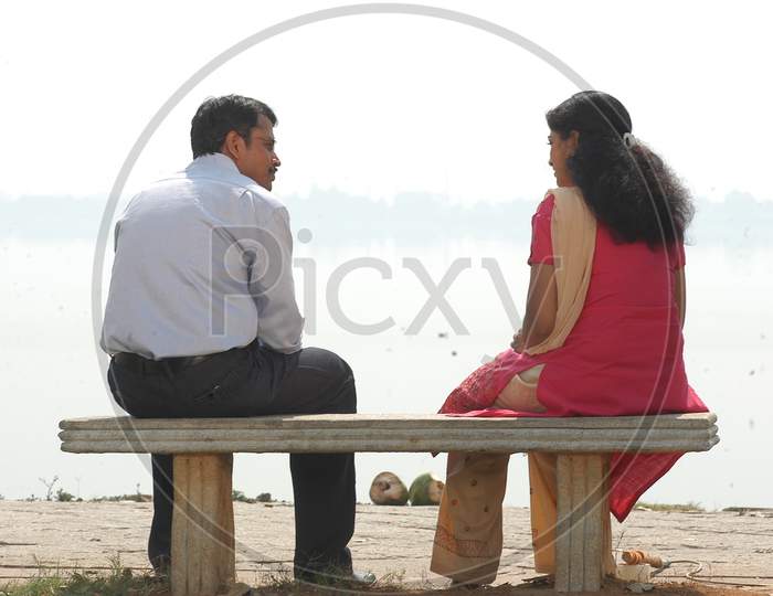 Young Lovers Couple Sitting at a Lake  And Taking With Each other