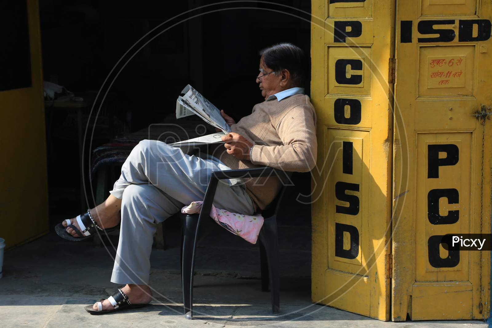 Indian Old Man Reading Newspapers outside a Telephone booth