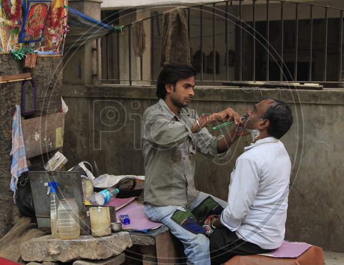 A Indian street barber giving his client a shave in a street