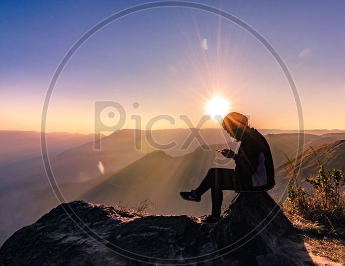 Young Indian Man using Mobile or Smartphone on Hill Top with Sun rays in Background