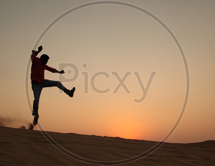 Silhouette of a man Jumping With Joy In Desert with a sunset In Background