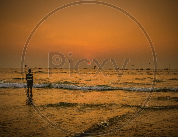 A person standing in beach at sunset time and ships moving in water
