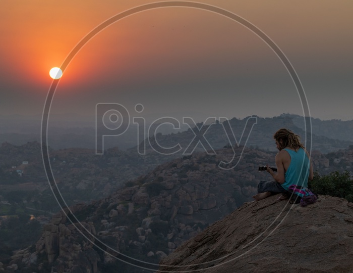 A man playing music on the hills of Hampi during Sunset