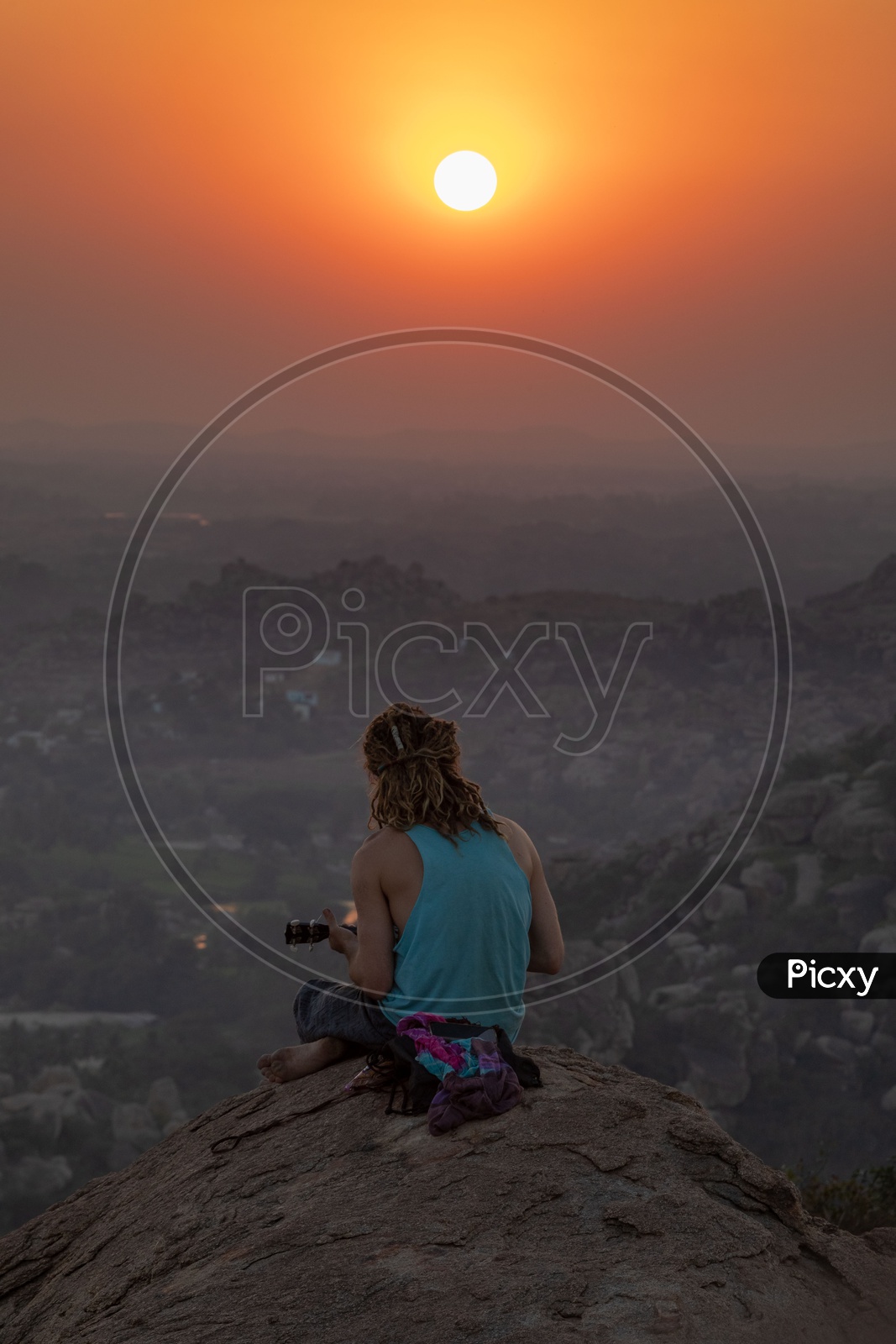 A man sitting on a hill and playing music during sunset in Hampi