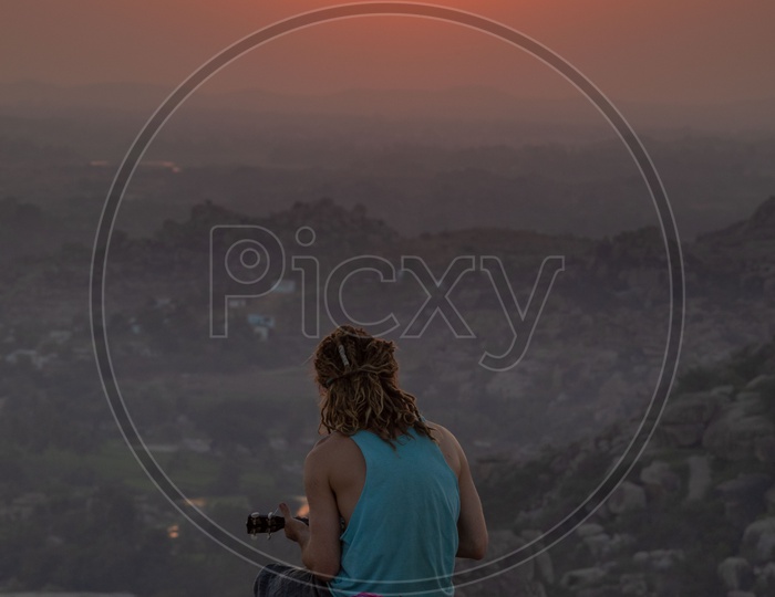 A man sitting on a hill and playing music during sunset in Hampi