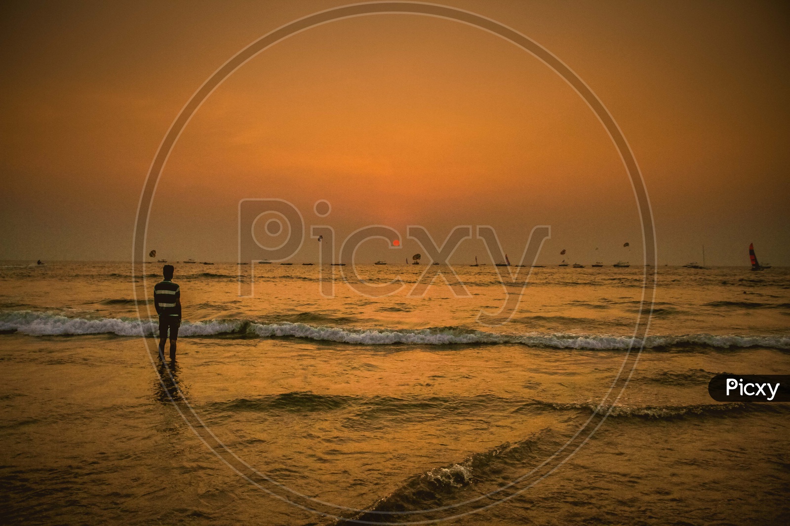 A person standing in beach at sunset time and ships moving in water