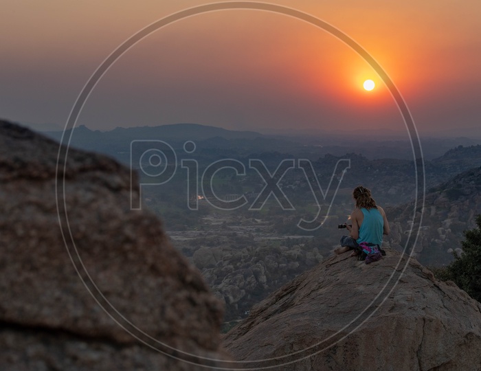 A man sitting a hill and playing music during sunset in Hampi