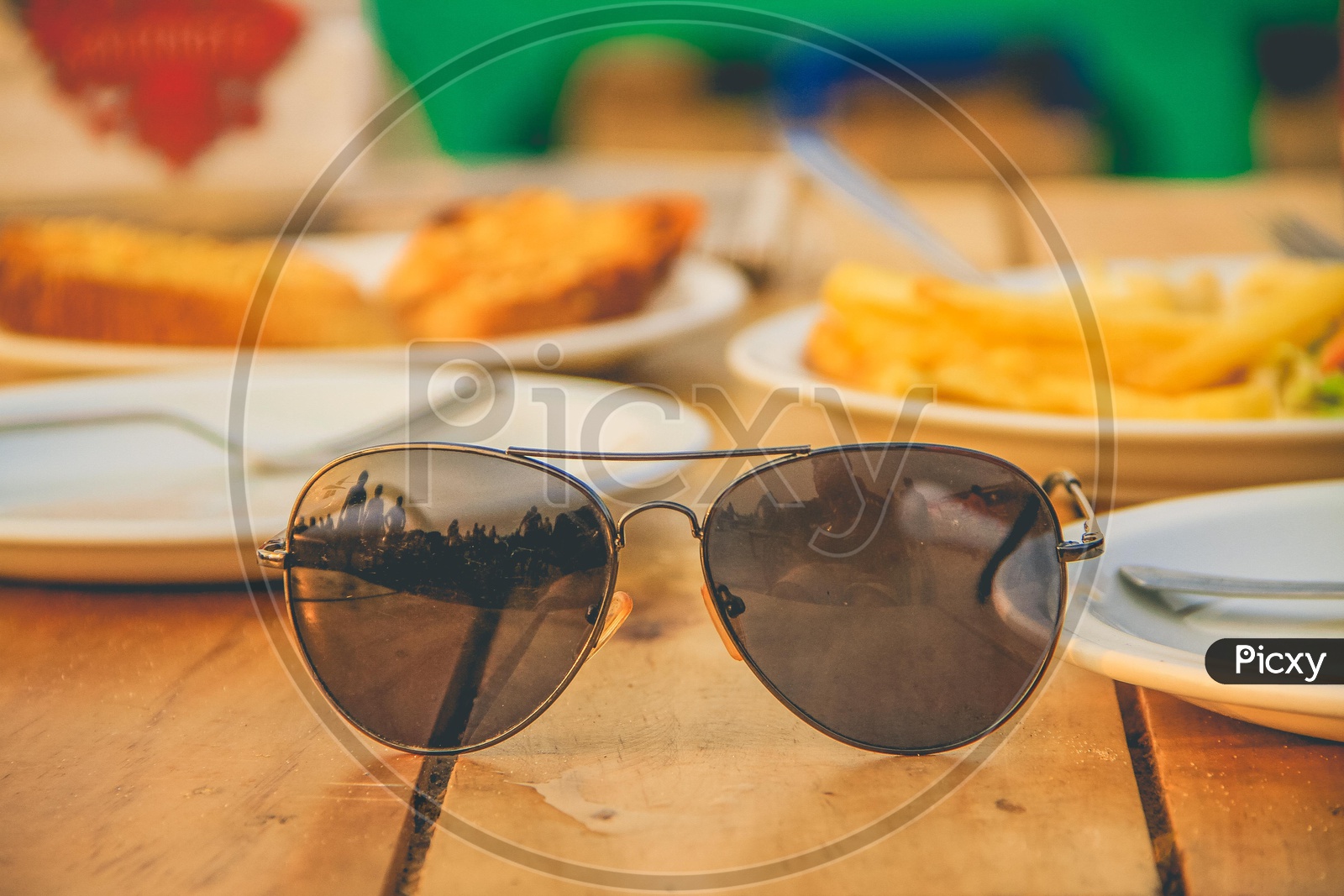 Sunglasses on a wooden table and food in the back