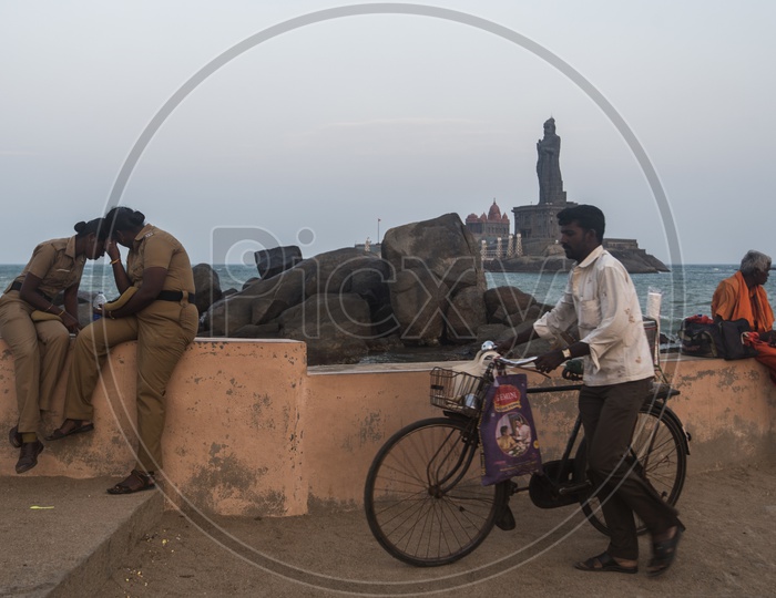 A man with a bicyle walking along the beach side. Indian women police.