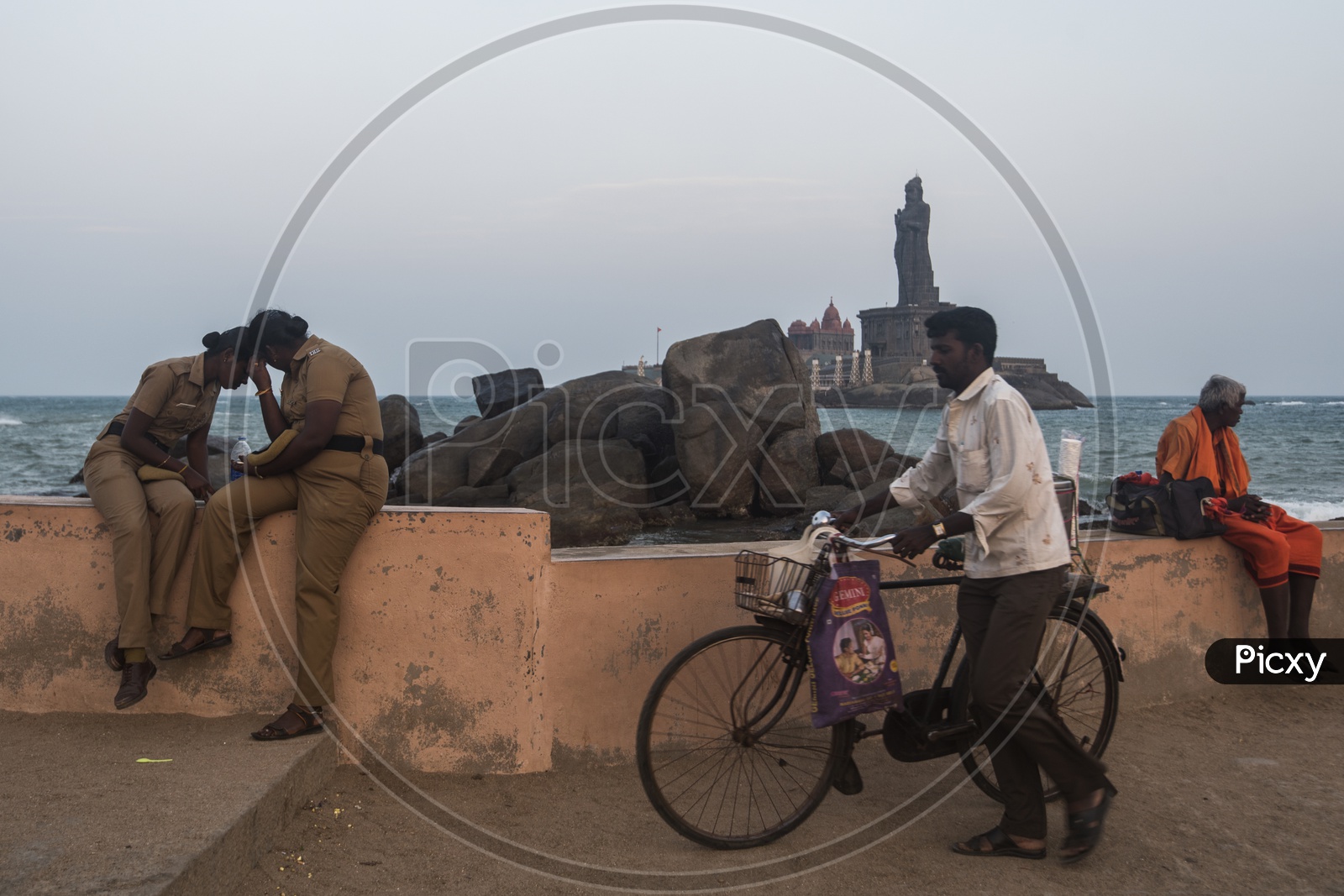 A man with a bicyle walking along the beach side. Indian women police.