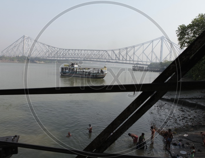 View of Howrah Bridge and people taking bath alongside the Hooghly River