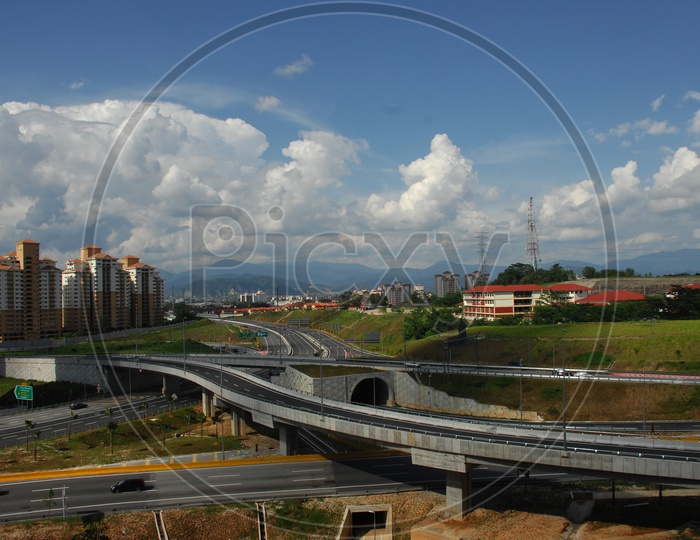 Aerial view of the roadways and overpass with buildings and blue sky covered clouds in background