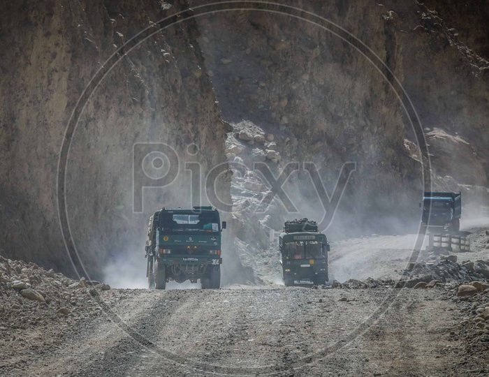 Army Trucks and Buses moving on the dirt road alongside the sanstone mountains