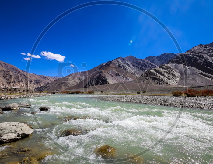 Flowing stream of a river alongside the mountains with blue sky