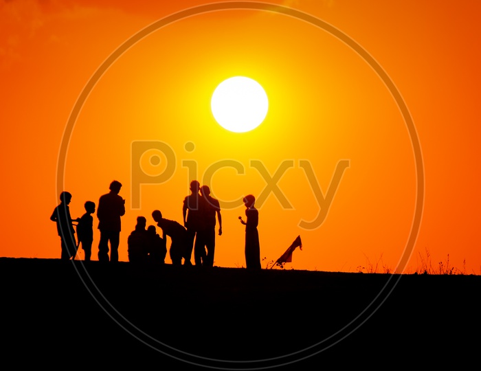 Silhouettes of Children On a Rock Hill With Golden Sun inBackground