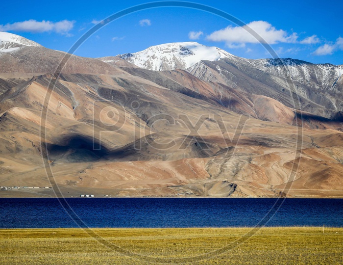 Landscape of Pangong Lake alongside the snow capped mountains covered with blue sky and clouds