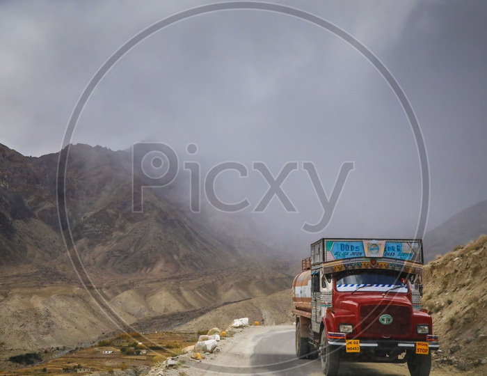 Lorry running on the rural road alongside the mountains with dark clouds covered in background