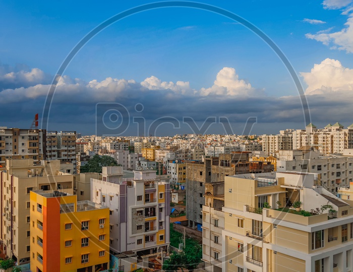 City Scape View With Apartments And Cotton Clouds In Blue Sky