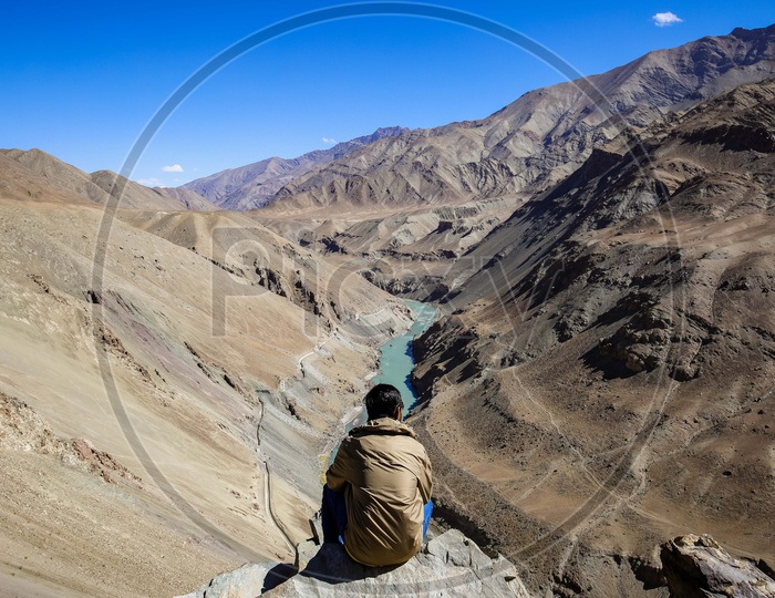 Man sitting on the cliff in front of the Indus River flowing in a Valley