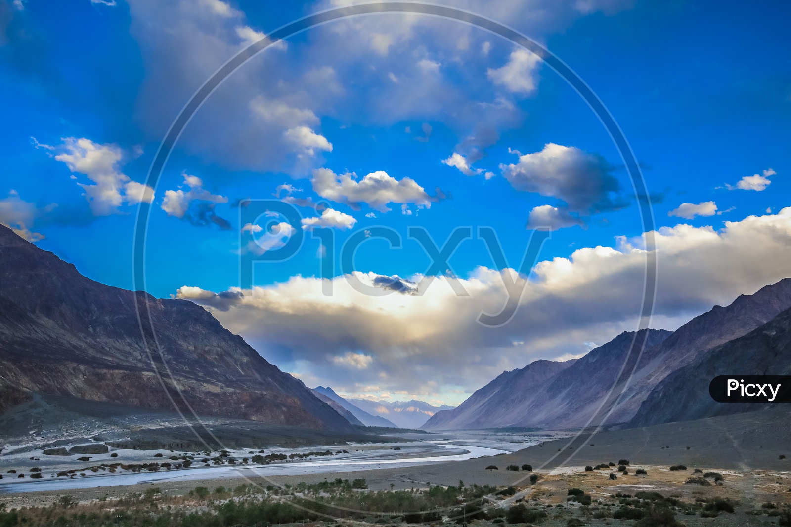 Landscape of a Zanskar river flowing through the mountains with blue sky and dramatic clouds in the background