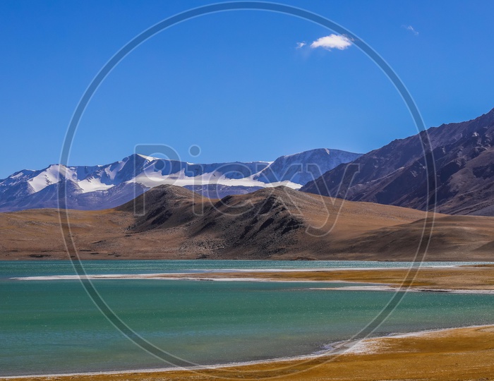 Landscape of snow covered mountains with blue sky alongside the Pangong Lake