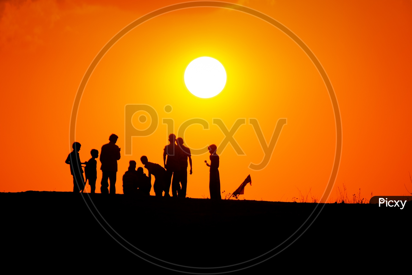 Silhouettes of Children On a Rock Hill With Golden Sun inBackground