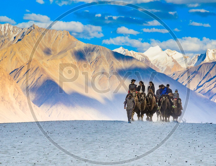 Travellers experiencing camel ride alongside the mountains