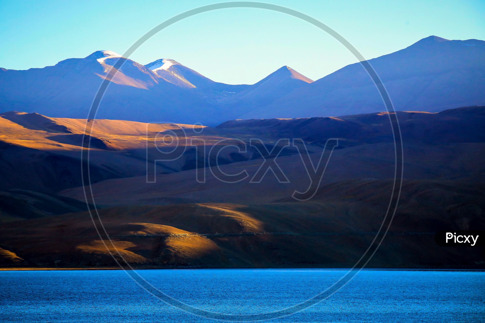 Landscape of snow capped mountains with sunlight alongside the Pangong Lake