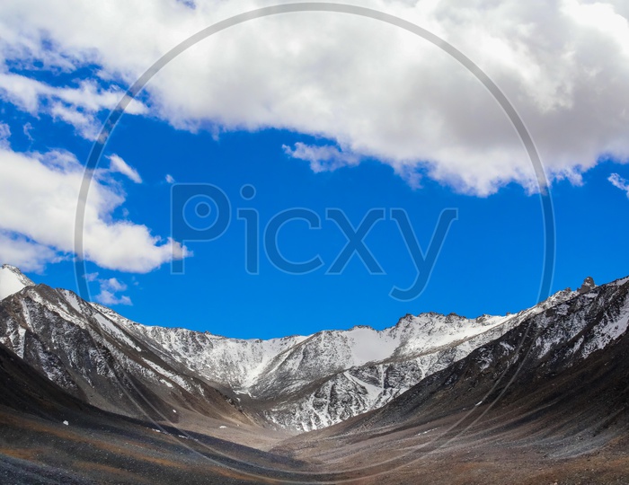 Snow covered Himalayan Mountains with blue sky and clouds in background