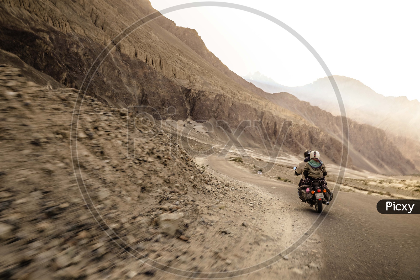 Two travellers riding motorcycle on the dirt road alongside the mountains