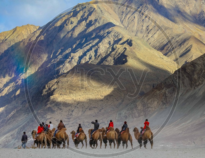 Travellers experiencing camel ride amidst of rainbow over the mountains
