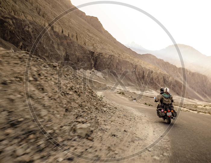 Two travellers riding motorcycle on the dirt road alongside the mountains