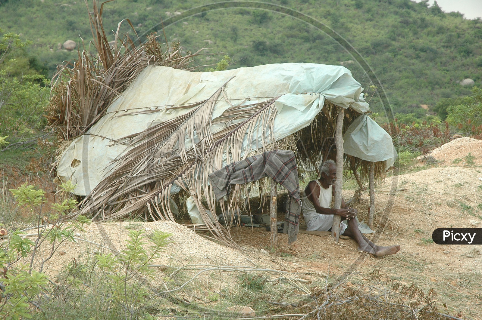 A man takes shelter in a small thatched hut
