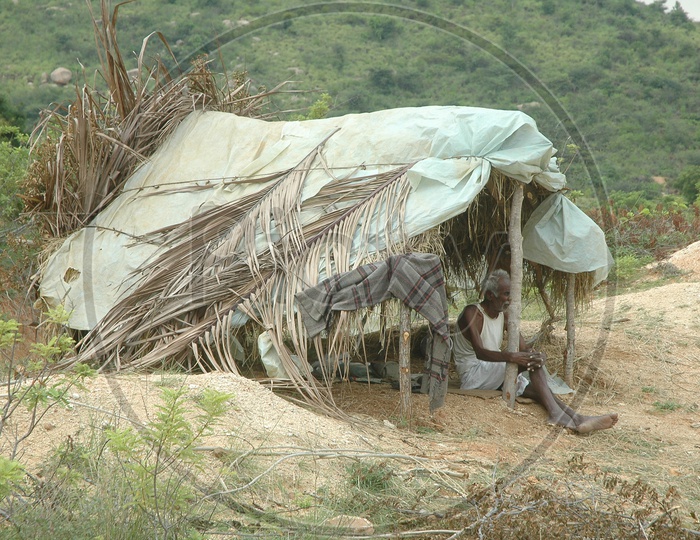 A man takes shelter in a small thatched hut