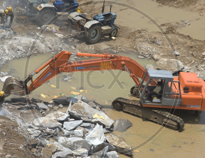 Bulldozer and the labourer excavating the massive rock bodies with the help of a heavy driller