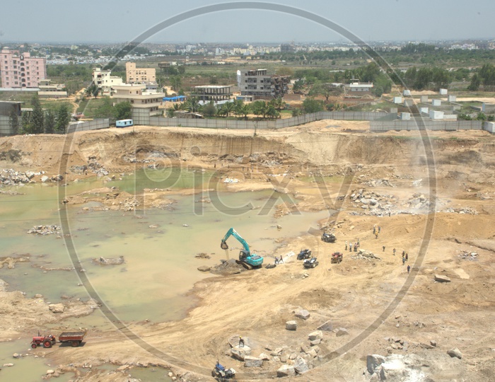Aerial view of Bulldozer excavating the rock bodies alongside the labourers drilling at a construction site