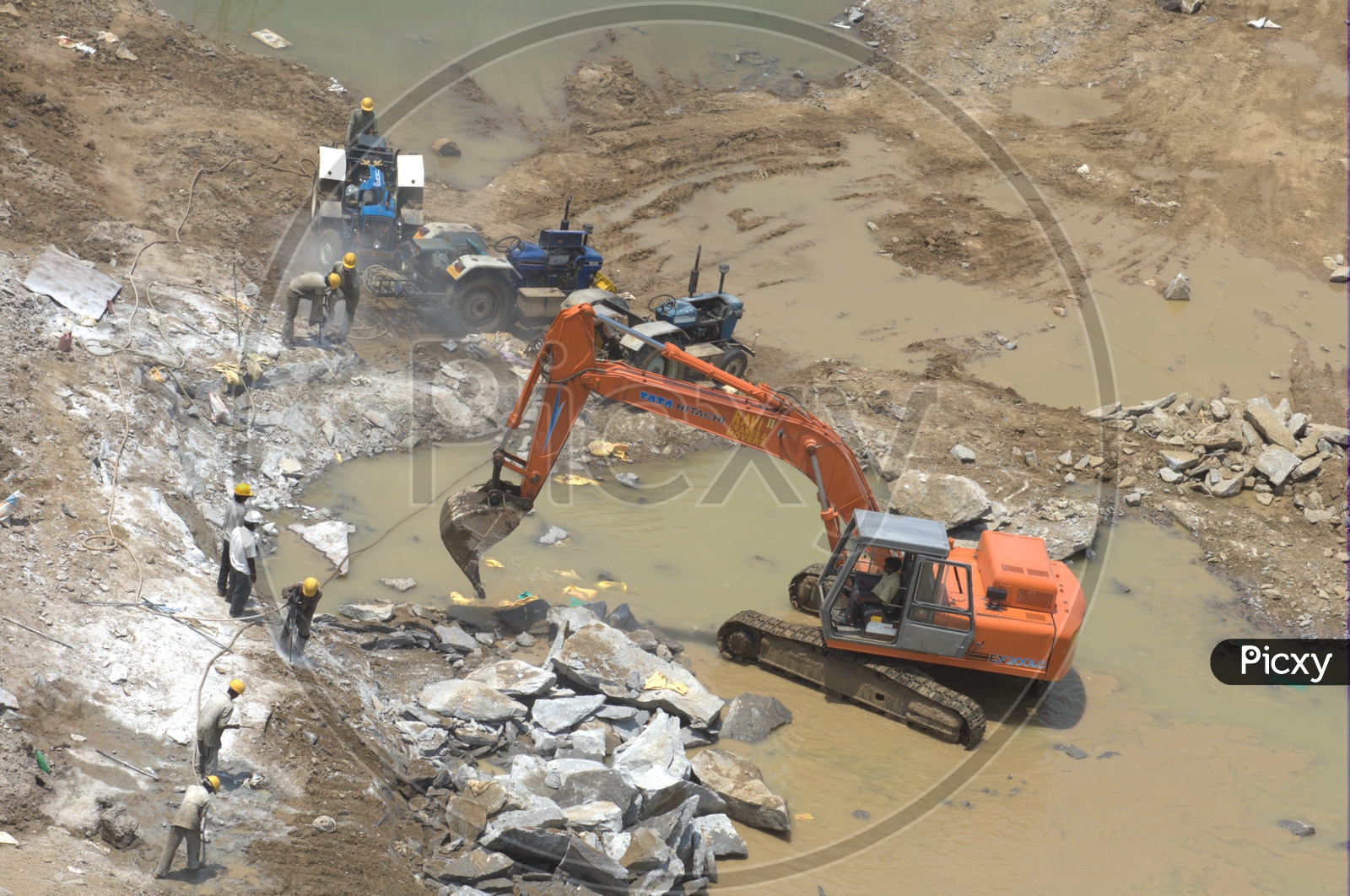 Bulldozer excavating the rock bodies alongside the labourers drilling in background at a construction site