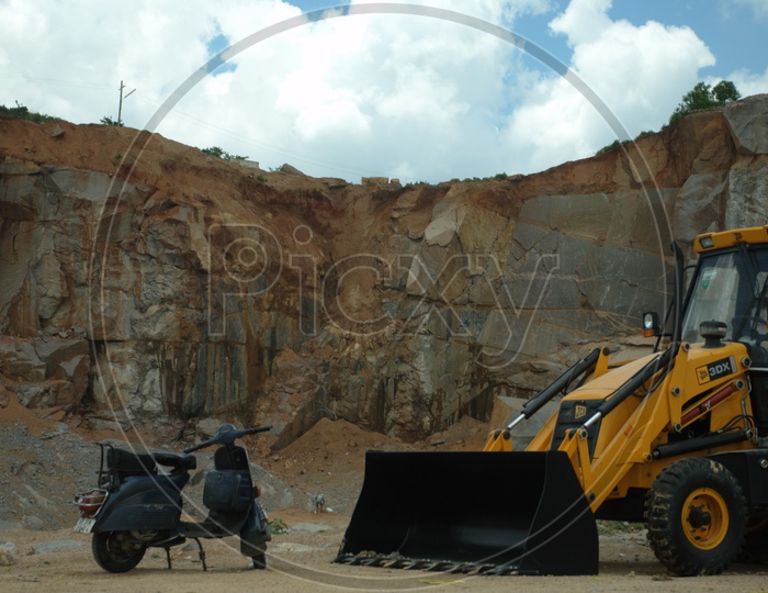 Chetak bike and a bulldozer alongside the excavation site with cloudy sky in background