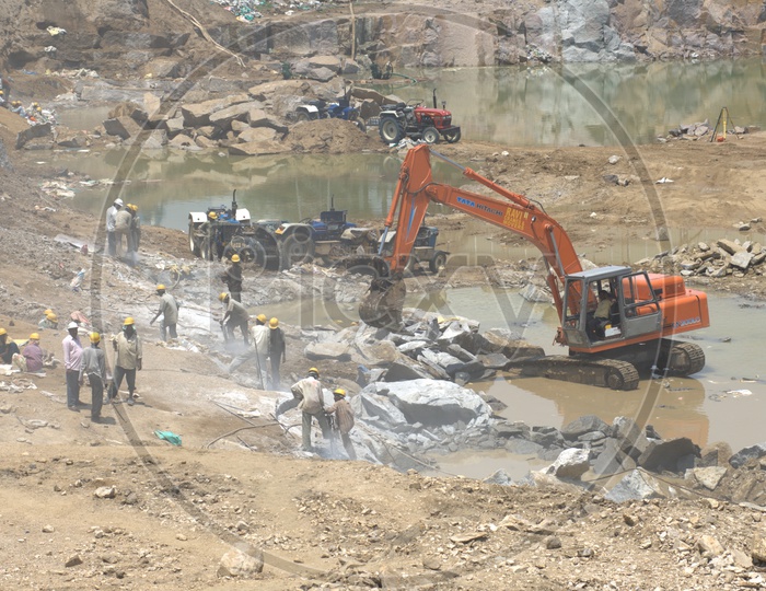 Bulldozer excavating the rock bodies alongside the labourers drilling at a construction site