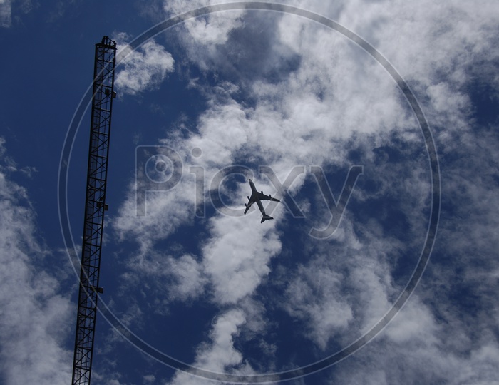 Aeroplane alongside the tower crane with  cloudy blue sky in background